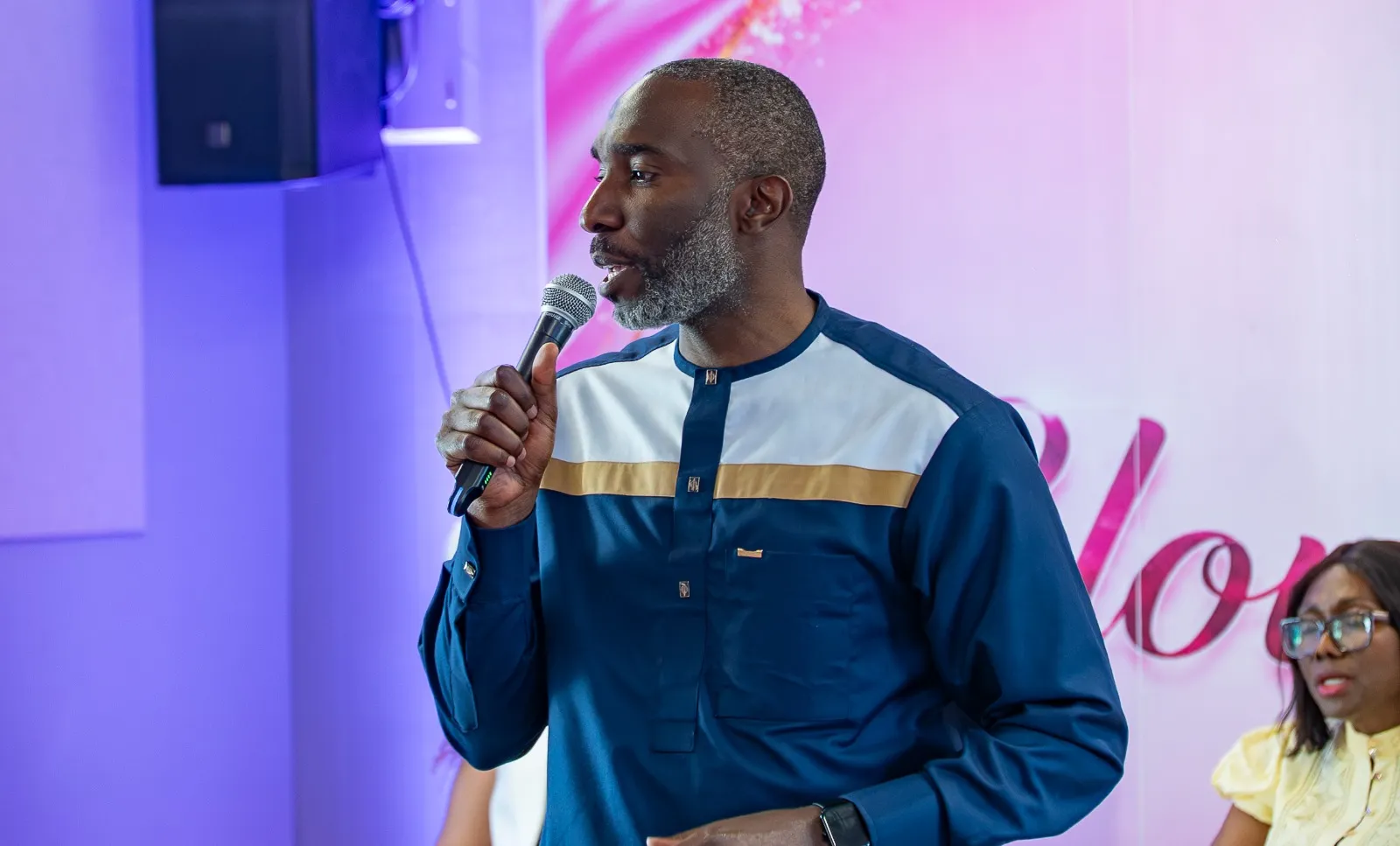 A man in navy and gold attire speaking into a microphone at a church gathering