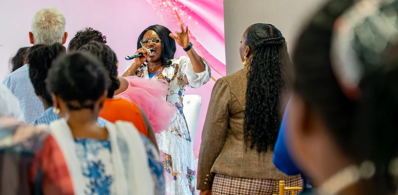 A woman leading worship with a microphone as the congregation stands and sings